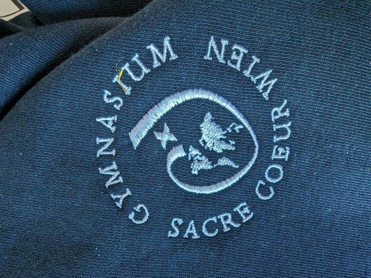 Besticktes Schullogo des Gymnasiums Sacré Coeur Wien auf einem dunkelblauen Sweater